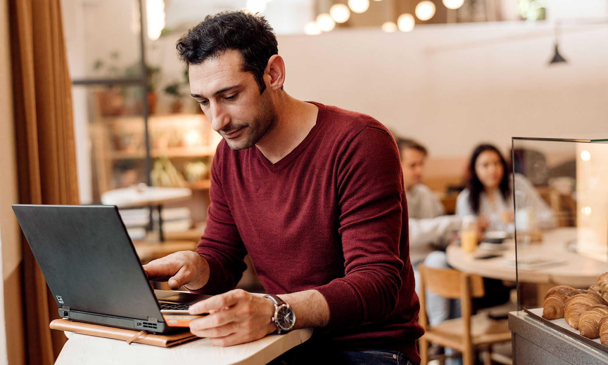 Man sitter i ett café med sin laptop och håller i ett betalkort